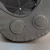 Close-up of a black cap with two gray circular speakers on a light gray background